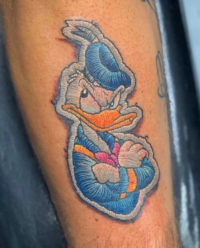 Full color donald duck crossstitch thread patch forearm tattoo by tattoo artist Russ Howie of Sacred Mandala Studio in Durham, NC.